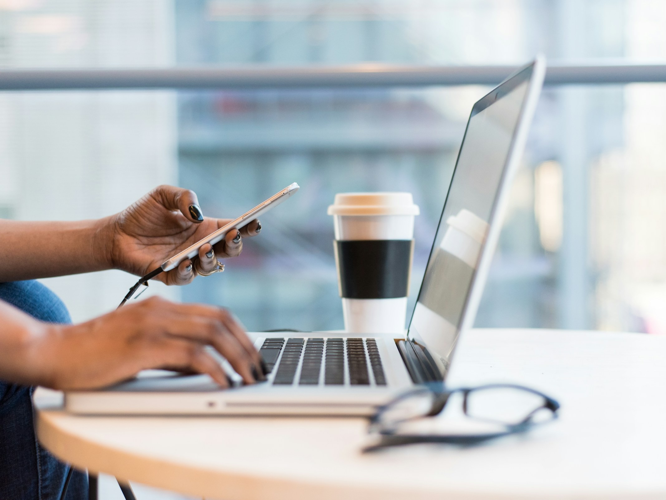 Photo of a person using their mobile smartphone while at a computer to illustrate the launch of OpenAI Operator that promises to democratise agentic AI by bringing agents into the browser.